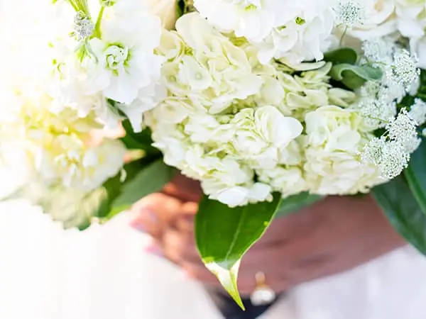Close-up of a bride holding a lush white wedding bouquet with hydrangeas and roses